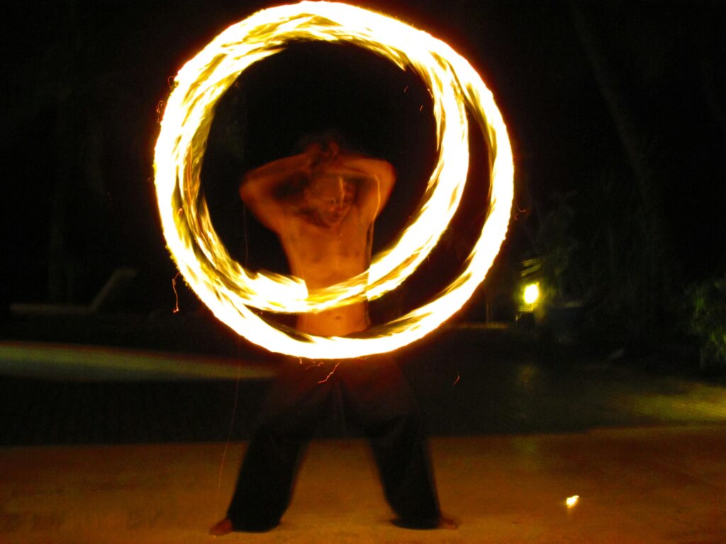 Shirtless performer creates dynamic spirals of fire against a night sky.